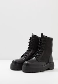 Schwarze Knöchelstiefel mit glattem Leder-Zeh, Obermaterial aus Stoff, Schnürung an der Vorderseite und dicker Gummisohle mit tiefem Profil für Traktion und Haltbarkeit.