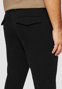 Schwarze Hose mit schlanker Passform und strukturiertem Stoff. Enthält Gesäßtaschen mit Klappen und ein dezentes Logo-Detail.