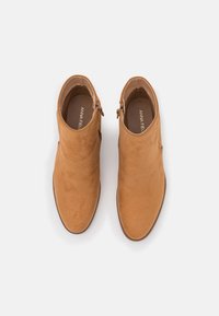 Brązowe zamszowe botki za kostkę o gładkiej fakturze, z bocznym zamkiem błyskawicznym i niskim, wyprofilowanym obcasem. Okrągły nosek i minimalne przeszycia.