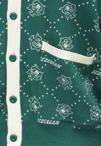 Cardigã verde com detalhes brancos, apresentando um padrão repetido de personagens caricaturais. Tem botões verdes e um bolso frontal.