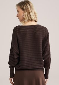 Pull en maille marron avec une coupe ample et oversize, composé de rayures horizontales et de poignets côtelés. Le matériau semble doux avec une finition texturée.