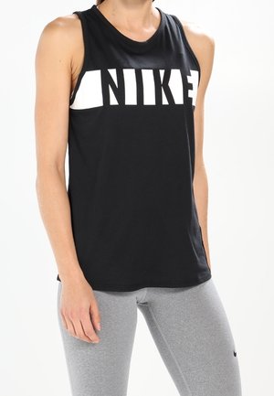 Femme portant un top Nike noir sans manches et des leggings gris clair, debout devant un fond blanc uni.