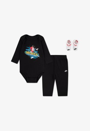Czarny body z długim rękawem z grafiką "Just Do It", dopasowane czarne spodnie oraz białe botki z czerwonymi akcentami i logo Nike.