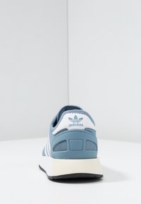 Blå sneakers i mesh och syntetmaterial, vita ränder och logotyp på hälen, vadderad sula, rundad form och texturerade detaljer.