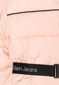 Jasnoróżowa kurtka puchowa z pikowaną fakturą, z czarnym pasem w talii z logo "Klein Jeans" oraz poziomą kieszenią na zamek z przodu.