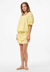 Top amarillo con estampado floral, mangas abullonadas y escote cuadrado, combinado con una falda corta con volantes. Tejido suave y ligero, diseño casual.