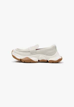 Chaussure slip-on gris clair avec semelle en caoutchouc épaisse blanche et marron, coutures style mocassin et large bride sur le dessus.