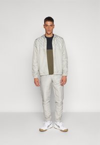 Chaqueta de cremallera gris claro con un diseño acolchado texturizado en los hombros, combinada con pantalones ajustados a juego y zapatillas blancas.