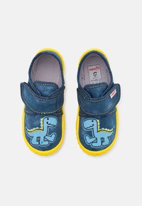 Zapatos infantiles azules y amarillos con diseños de dinosaurios en la parte frontal y correas de velcro para sujetar, mostrados desde arriba sobre un fondo blanco.