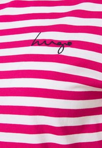 Camiseta a rayas rosa y blanca de tejido ligero. Presenta un logo bordado en negro "hugo" en el centro.