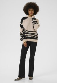 Un pull oversized beige et noir à rayures en matière pelucheuse, associé à un pantalon noir à jambe droite et des escarpins pointus à motif zèbre.