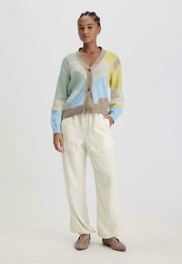 Monivärinen neulecardigan, jossa on sinisen, beigen ja keltaisen sävyjä, V-pääntie ja napitus. Yhdistetty vaaleisiin kermaisiin housuihin.