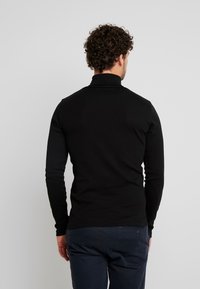 Schwarzes Langarm-Poloshirt mit körperbetontem Design, aus glattem Material gefertigt, mit hohem Kragen und flachen Nähten.