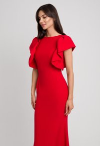 Czerwona dopasowana sukienka z falbankowymi rękawami, wykonana z gładkiego materiału. Posiada dekolt łódkowy i elegancką sylwetkę, sięgającą do podłogi.