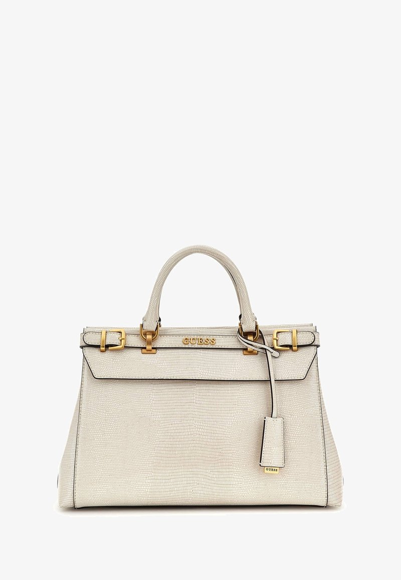 Sac à main en cuir texturé couleur crème avec boucles dorées et logo Guess, deux poignées et une étiquette suspendue sur fond blanc.