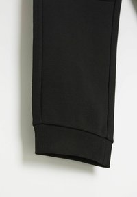 Czarne dresowe spodnie z miękkiego materiału, zakończone ściągaczem, z żebrowanym wykończeniem na dole. Prosty design bez widocznych wzorów czy akcesoriów.