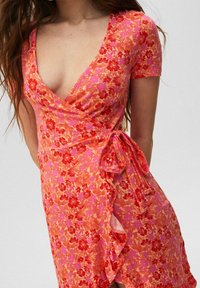 Vestido envolvente floral en vibrante naranja y rosa, con mangas cortas, escote en V profundo y un detalle de lazada en la cintura con un dobladillo con volantes.