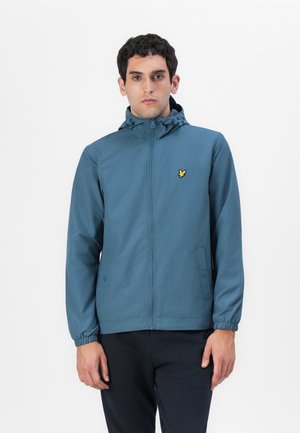 Veste légère à capuche en turquoise avec des poignets élastiques, fermeture éclair et un petit logo jaune sur la poitrine. Texture lisse et design décontracté.