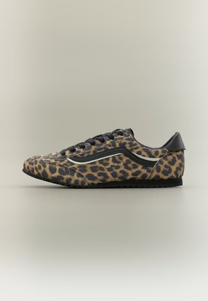 Zapatilla de hombre de corte bajo con estampado de leopardo, cordones negros, suela negra y detalle de cuero negro en el talón.