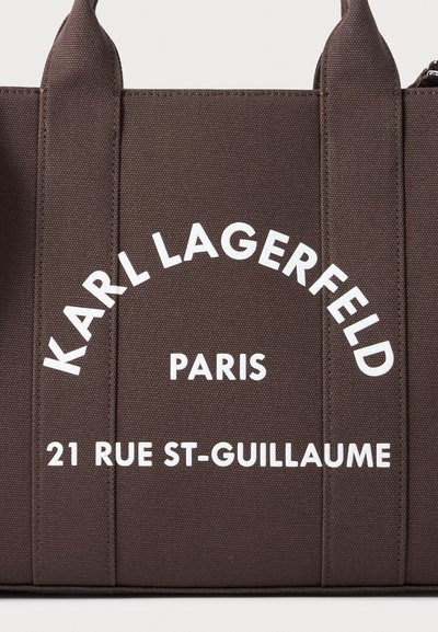 Близък план на тъмнокафява платнена чанта с бели надписи: Karl Lagerfeld Paris, 21 Rue St-Guillaume.