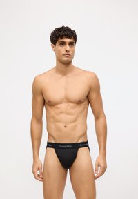 Czarny bawełniany thong z elastycznym pasem w miękkim wykończeniu z logo Calvin Klein. Dopasowany krój, gładka tekstura.