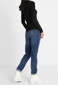 Schwarzes Langarmshirt kombiniert mit blauen Jeans und weißen Stiefeletten. Die Jeans haben eine schmale Passform mit hochgekrempelten Säumen und sind aus Denim gefertigt.