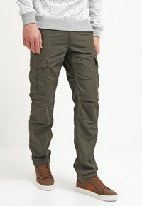 Oliven grønne cargo-bukser med flere lommer, letvægtsstof, afslappet pasform og opsmøgede nederkanter, parret med brune højhælede sneakers.