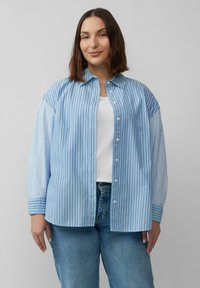 Hellblau-weiße gestreifte, übergroße Bluse mit Knopfverschluss, ausgestattet mit Kragen und umgeschlagenen Ärmeln, kombiniert mit blauen Jeans.