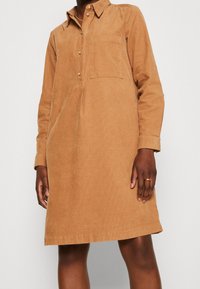 Braunes Cordkleid mit langen Ärmeln, Knopfkrause, Brusttasche und einer lockeren Passform, endet oberhalb des Knies und verfügt über eine dezente Textur.