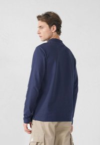 Camicia a manica lunga blu navy con collo rotondo, realizzata in cotone, con orli cuciti e spacchi laterali per il comfort.