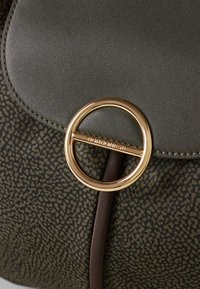 Green textured bag with a gold circular clasp. Brown accents and a subtle pattern dominate the fabric. Smooth leather flap on top.