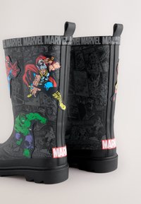 Svarta gummistövlar med seriefigursgrafik av Marvel-superhjältar, med ett texturerat mönster och framträdande röd "MARVEL"-logotyp.