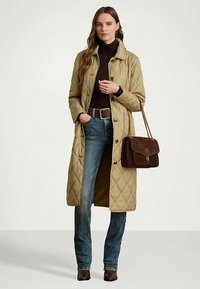 Moteris vilkinti smėlio spalvos gilią striukę, juodą golfą, mėlynus džinsus, rudus batus ir nešanti tamsiai rudą rankinę su auksiniu grandininiu dirželiu.