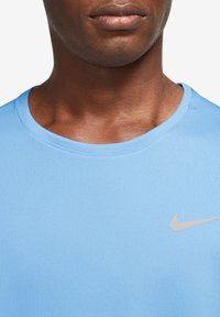Sinine sportlik särk, mis on valmistatud tekstureeritud kangast, ümara kaelusega ja vasakul küljel on silmapaistev hall Nike logo.