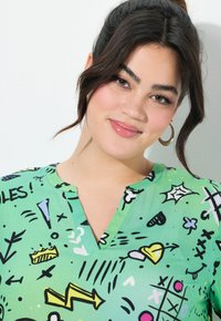 Kurzärmlige grüne Bluse mit verschiedenen verspielten schwarzen und bunten grafischen Mustern, im V-Ausschnitt-Design und aus leichtem, glatten Material.
