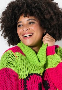 Pull en tricot coloré avec des rayures vertes, roses et noires. Design à col montant avec un fil texturé et des mailles lâches.