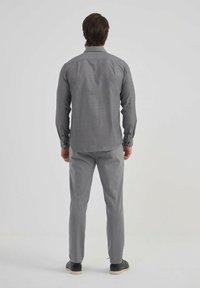 Chemise grise à boutons avec des manches longues et un ourlet droit, associée à un pantalon gris slim, vue de dos.