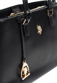 Černá kožená kabelka s texturovaným povrchem, zdobená zlatými detaily a přívěskem s postavičkou. Zapínání na zip a dvojité horní držadlo.