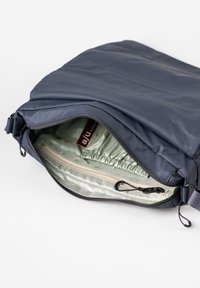 Borsa a spalla in tessuto blu navy con chiusura con zip. L'interno presenta una fodera verde chiaro, una tasca arricciata e un compartimento con zip beige.