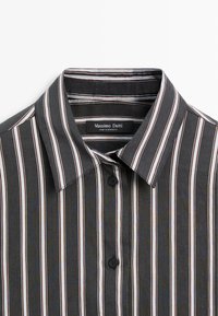 Chemise à rayures verticales noires, blanches et marron avec col et deux boutons noirs, affichant l’étiquette « Massimo Dutti » à l’intérieur du col.