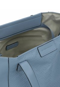 Borsa tote azzurro chiaro con un motivo geometrico testurizzato, caratterizzata da un bordo superiore liscio, una tasca interna con zip e un'etichetta con logo.