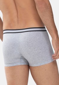 Mandens nederste ryg og ben iført lysegrå boxer shorts med en sort og hvid stribet talje mod en ensfarvet baggrund.