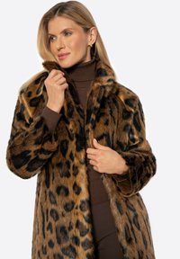 Kabát z umělé kožešiny s leopardím potiskem, měkkou texturou, hnědou a černou barvou, s širokým límcem a volným střihem, nošený přes hnědý rolák.