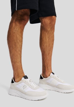 Fehér és világosszürke sneaker fekete sarok részletekkel, suede és hálós anyagokból, fűzős kialakítással, és logó részletekkel az oldalon.