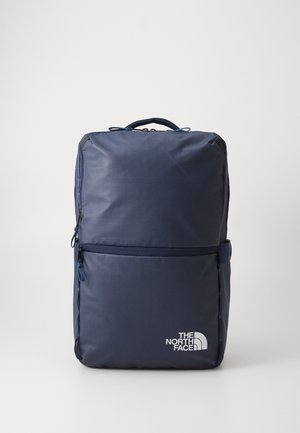Sac à dos rectangulaire bleu foncé avec poignée supérieure, poche zippée frontale et logo "The North Face" blanc dans le coin inférieur droit.