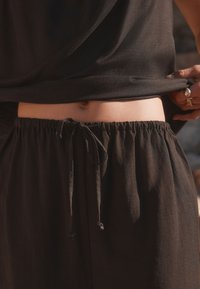 Black, lightweight pants featuring an elastic waistband with a drawstring. The texture is soft, with a relaxed fit around the waist.