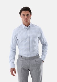 Hellblau und weiß kariertes Button-Up-Hemd aus Baumwolle, kombiniert mit grauen, gefalteten Wollhosen. Enthält eine Brusttasche und Manschetten.