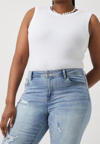 Vit ribbad linne med breda ärmhål, tillsammans med ljusblå högmidjade jeans med slitna detaljer.