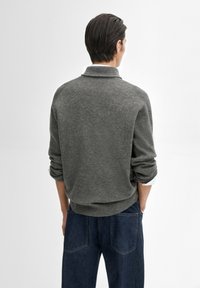 Grijze gebreide trui met een kraag, geribbelde textuur en omgerolde mouwen, gecombineerd met donkerblauwe denim jeans. Minimalistisch ontwerp.