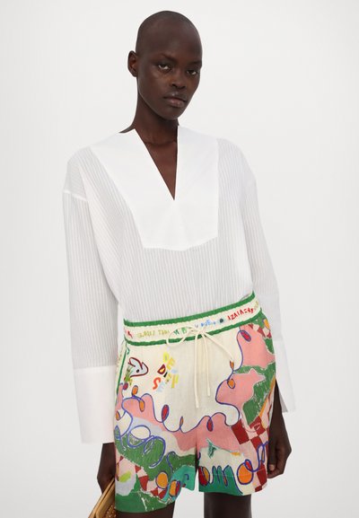 Witte katoenen blouse met een diepe V-hals en lange mouwen; gecombineerd met multicolore shorts met abstracte patronen en een trekkoord in de taille.